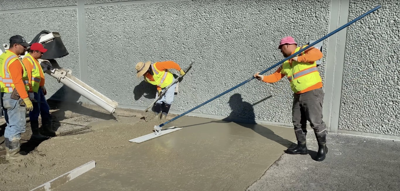 Concrete crew leveling a fresh commercial concrete slab at a job site in Texas